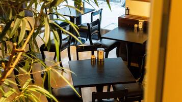 Un interior de restaurante con zona de comedor, sillas, mesas y una planta en maceta.