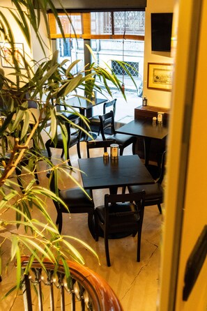 Un interior de restaurante con zona de comedor, sillas, mesas y una planta en maceta.