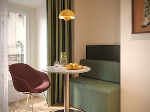 Un espacio habitable pequeño con una mesa redonda, una silla roja, un sofá, una cortina verde a rayas y una lámpara colgante amarilla.