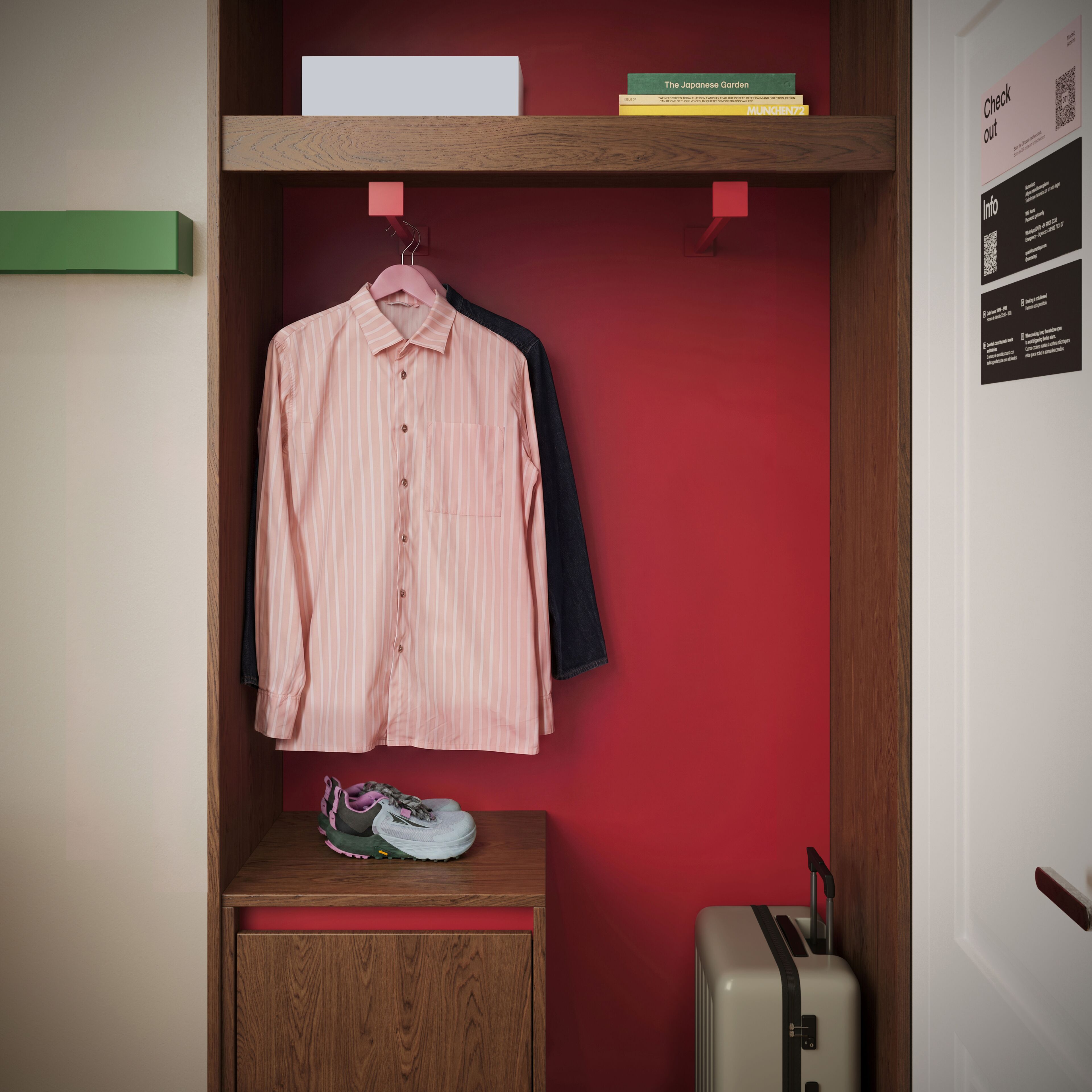 A room with a red wall, a wooden cabinet, a hanging shirt, and a suitcase.