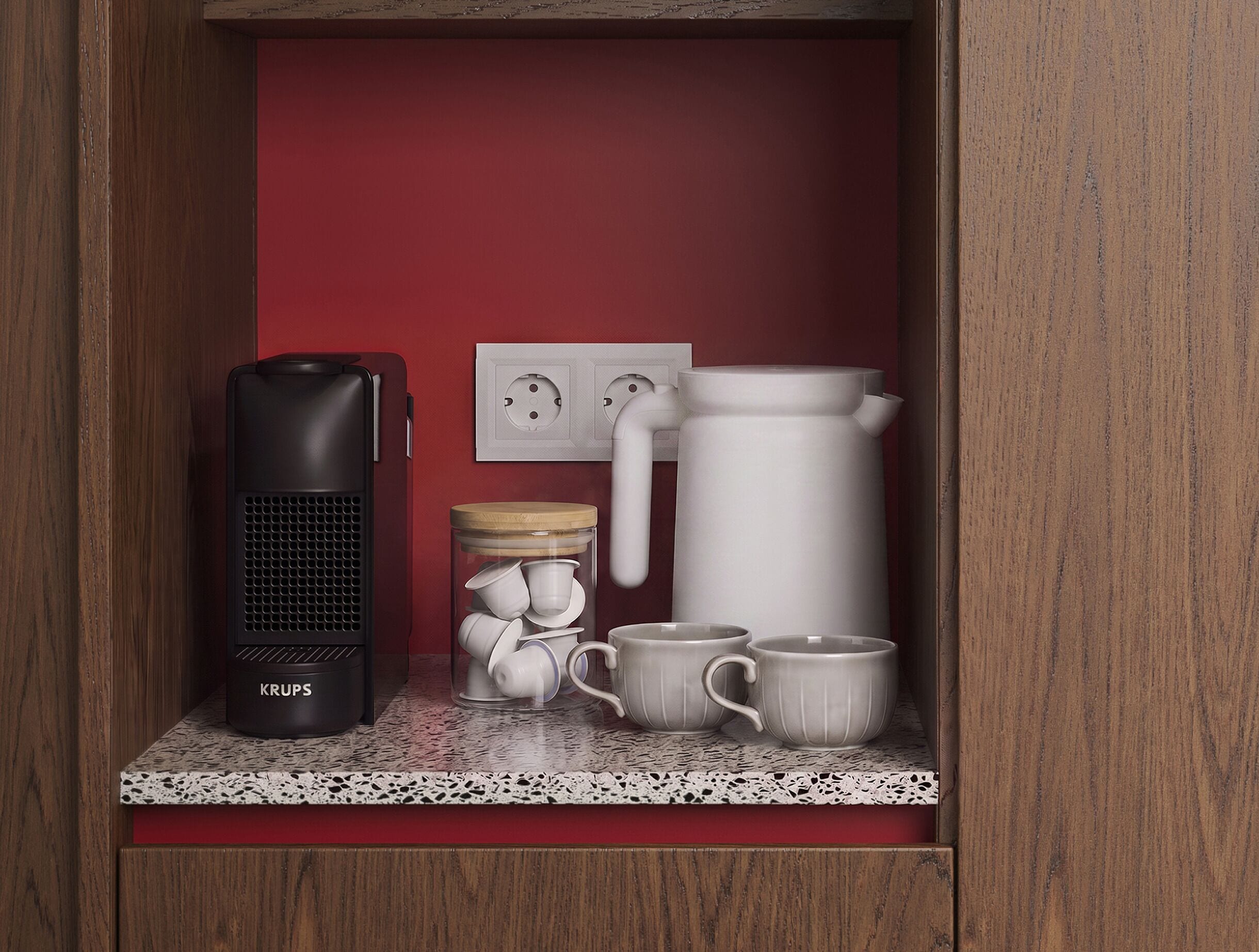 Una kitchenette equipada con cafetera, hervidor, un tarro con tazas y un enchufe.
