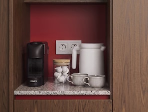 Una kitchenette equipada con cafetera, hervidor, un tarro con tazas y un enchufe.