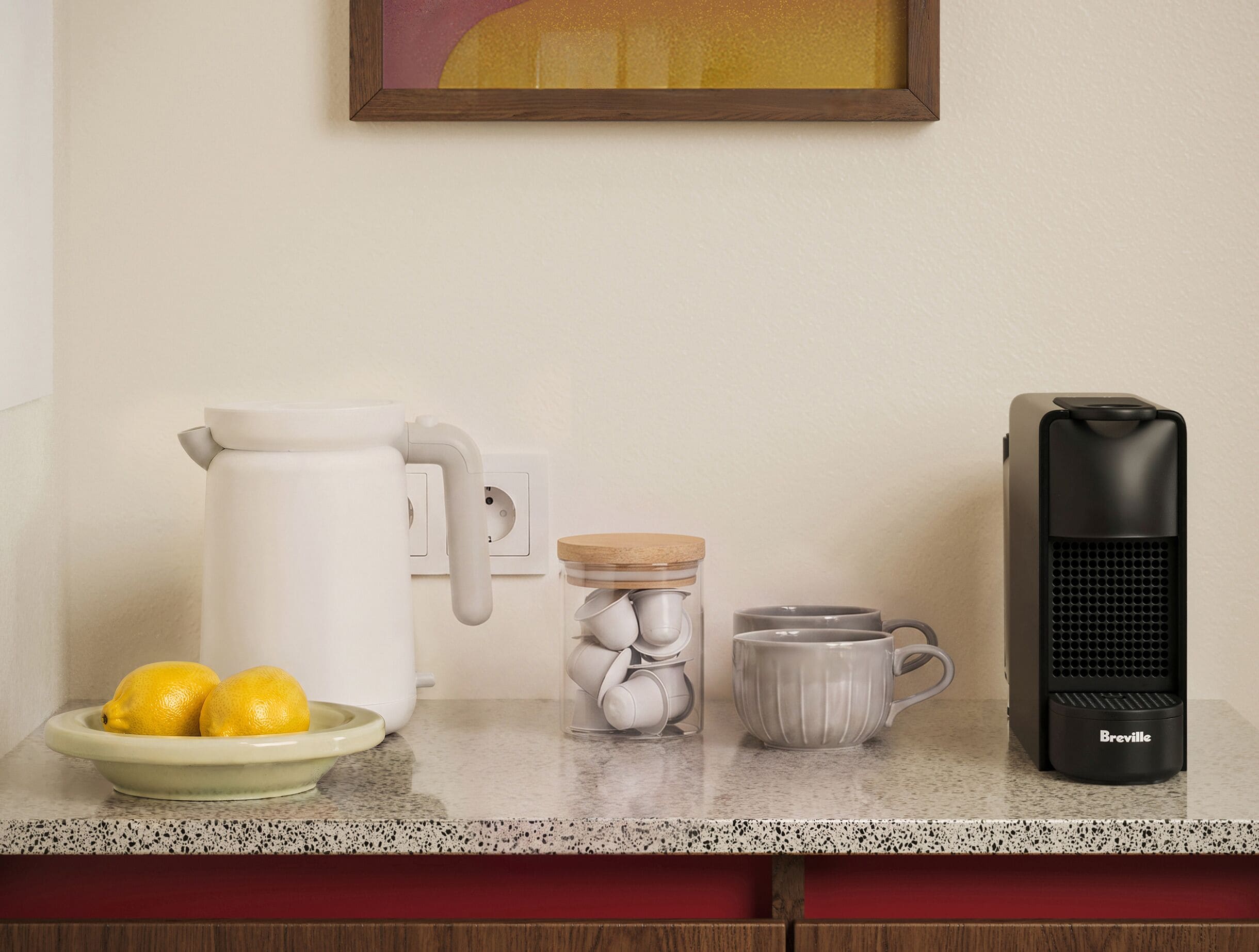 Una encimera de cocina con cafetera, hervidor, taza y limones en un plato.