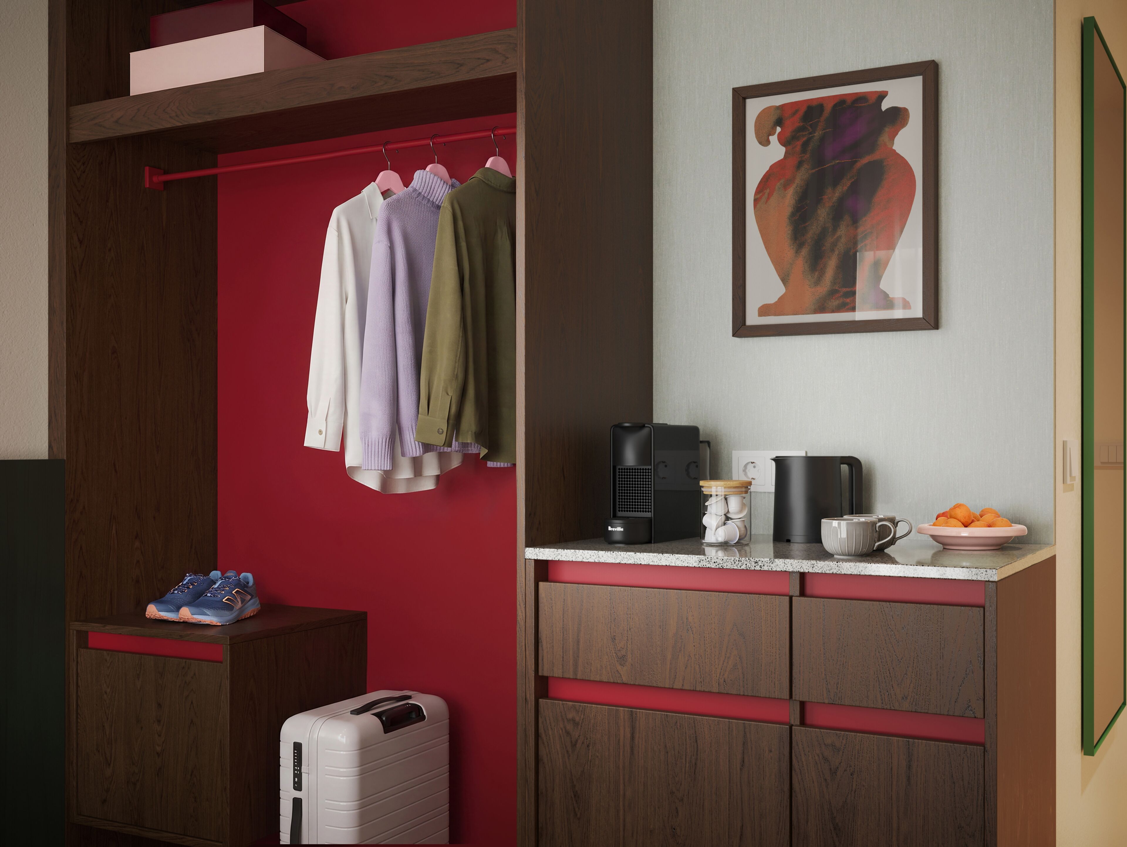 Quarto com parede vermelha, um armário de madeira, cabideiro com várias peças de roupa, cafeteira, caneca e uma tigela de frutas.