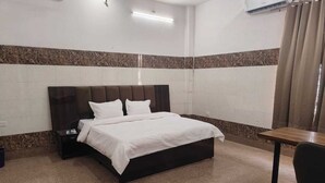 A hotel room with a bed, a nightstand, a table, and a chair. - The Hotel Junction Palace  (Aligarh)