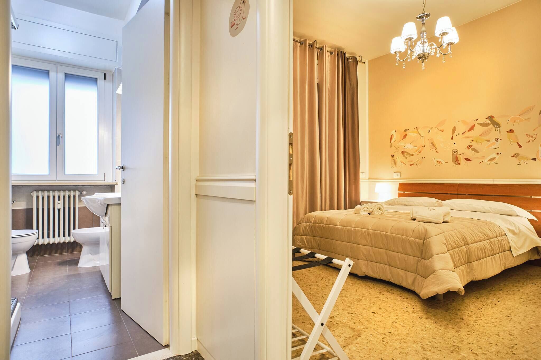 A hotel room with a bed, a radiator, a window, and a wall with bird illustrations.