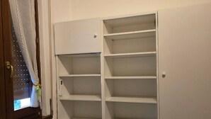 Un moble blanc d'emmagatzematge amb diverses prestatgeries i calaixos, situat al costat d'una finestra amb cortina.