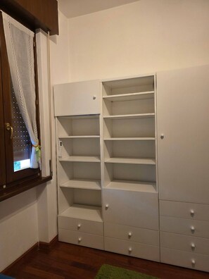 Ein weißer Stauraum mit mehreren Regalen und Schubladen, neben einem Fenster mit Vorhang.