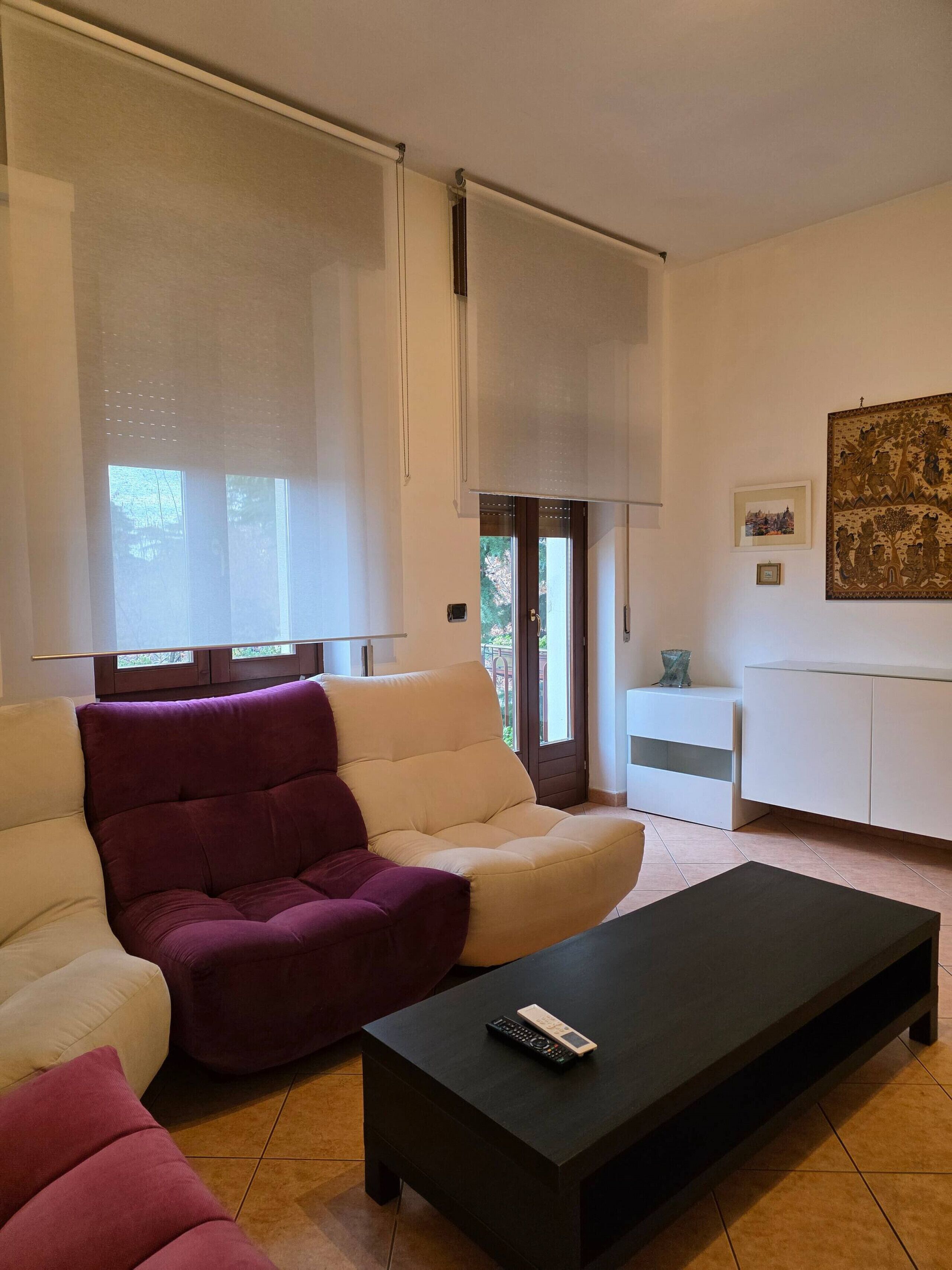 Un salon avec un canapé beige, un fauteuil violet, une table basse noire et un meuble blanc.