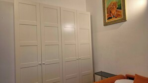 Un dormitori amb un armari blanc ampli, una taula petita, un llit amb roba de llit taronja i blanca, i un quadre encimbellat a la paret.
