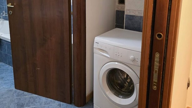 Una sala de bugaderia amb una màquina de rentar, una porta de fusta i un paviment de rajoles.