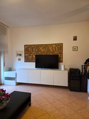 A living room with a flat-screen TV on a white entertainment unit, a large tapestry on the wall, and a black speaker system. - Maison Galliano  Verona (Verona)
