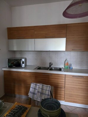 Eine Küche mit Holzschränken, einer Mikrowelle, einem Spülbecken und einem Geschirrgestell.