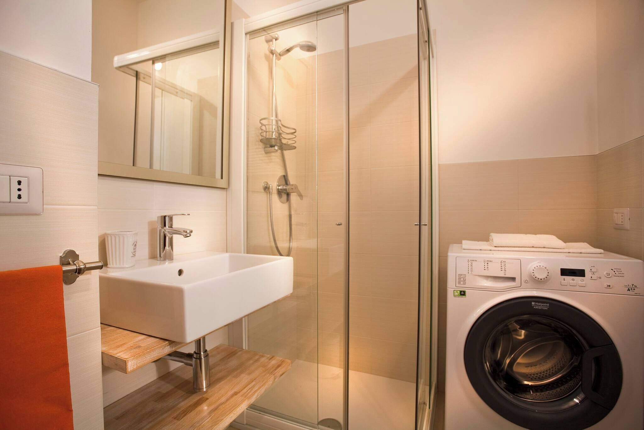 Un baño moderno con cabina de ducha de vidrio, un lavabo blanco y una lavadora de carga frontal.