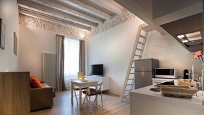 Un apartamento moderno con techo a la altura de un loft, zona de comedor, sala de estar con sofá, televisión, refrigerador y microondas.