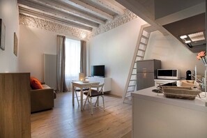 Eine moderne Wohnung mit Schlafgalerie, Essbereich, Wohnzimmer mit Sofa, Fernseher, Kühlschrank und Mikrowelle.