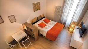 Una habitación de hotel pequeña con cama, escritorio, silla, radiador y televisión.