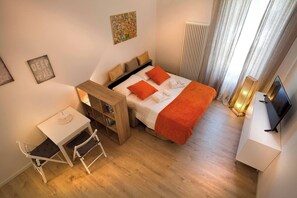 Ein kleines Hotelzimmer mit einem Bett, einem Schreibtisch, einem Sessel, einer Heizung und einem Fernseher.
