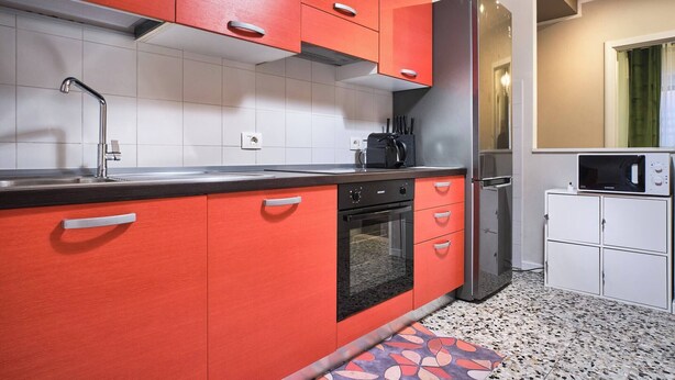 Eine moderne Küche mit roten Schränken, einer Edelstahl-Spüle, einem eingebauten Backofen, einem Kühlschrank und einer Mikrowelle.