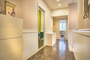 Un pasillo estrecho con una zona de cocina en un lateral, una silla verde y un radiador al fondo.