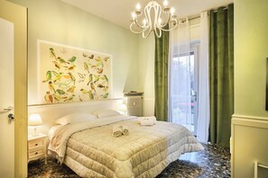 Une chambre d’hôtel avec un lit, un radiateur, un lustre et une grande fenêtre avec des rideaux.
