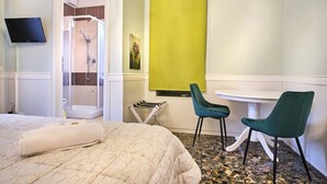 Quarto de hotel com cama, chuveiro, televisão e uma pequena mesa com cadeiras.