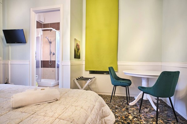 Una habitación de hotel con cama, ducha, televisión y una pequeña mesa con sillas.