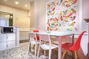 A modern kitchen with white cabinets, a microwave, a dining table with red chairs, and a wall mural of birds. - Stanza verde con bagno privato - uso cucina - La Voliera (Verona)