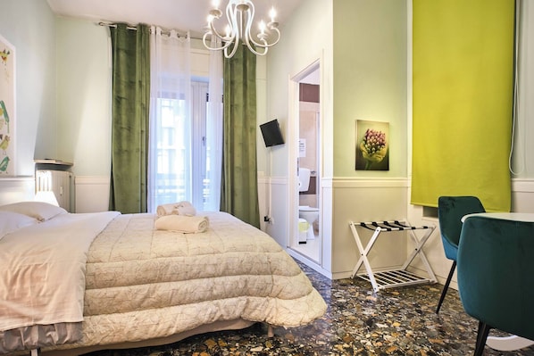 Quarto de hotel com cama, uma cadeira, mesa pequena, área de chuveiro e parede verde.