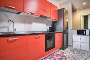 Una cocina moderna con armarios rojos, un lavamanos de acero inoxidable, horno empotrado, refrigerador y microondas.