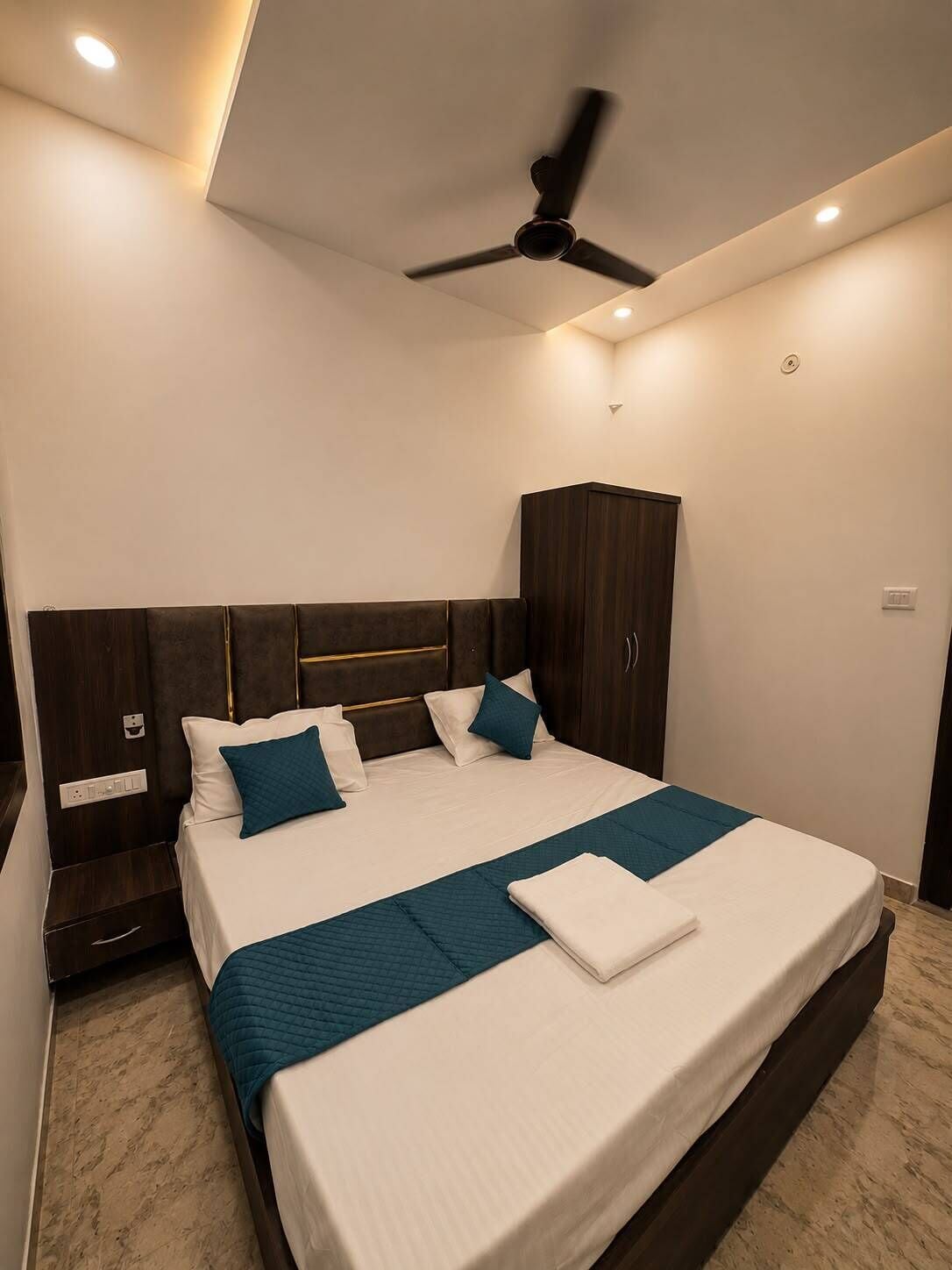 Una habitación de hotel moderna con una cama grande, cabecera de madera oscura y ventilador de techo.