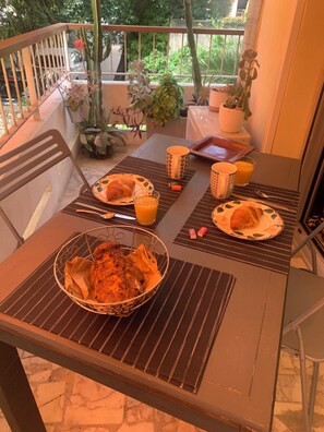 Una mesa de comedor con platos, vasos y una cesta de pan, rodeada de sillas y plantas en macetas.