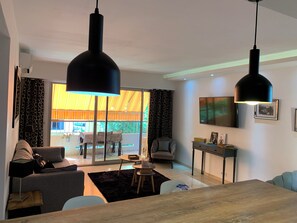 A modern living room with a sofa, a dining table, and a TV mounted on the wall. - Apartment, 2 bedrooms, air-conditioned, bathroom, kitchen, living room, terrace (Le Cannet)