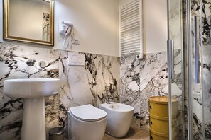 Et badeværelse med en marmorvæg, en konsolvask, et toilet, en bidet og en skraldespand i guld.