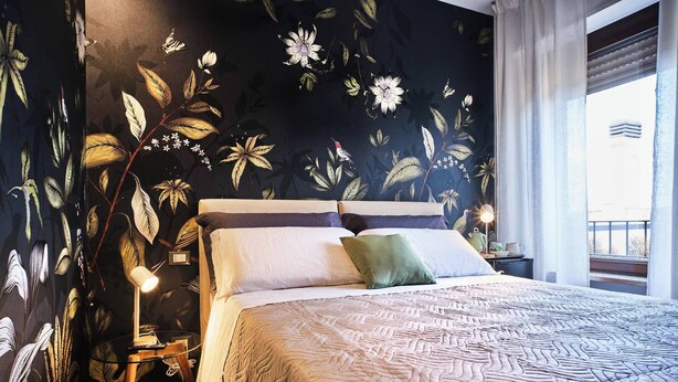 Een slaapkamer met een groot bed, een nachtkastje, een lamp en een raam met gordijnen.