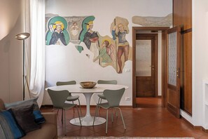 A dining area with a round table and chairs, a wall mural, and a door leading to another room. - Maison Riva 12 Verona (Verona)