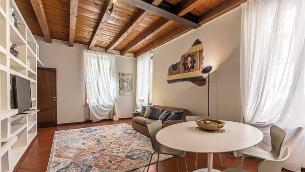 A living room with a wooden ceiling, a sofa, a coffee table, and a TV on a shelf. - Maison Riva 12 Verona (Verona)