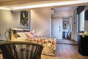 A bedroom with a bed, a chair, a desk, and a bathroom visible through an open door. - Maison Bra 10 - Purple (Verona)