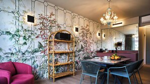 Een eetgedeelte met een tafel, stoelen, een rode bank, een bamboeboekenkast en een wand met een bloemenmotief.
