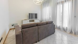 A modern living room with a grey sofa, a flat-screen TV on a white cabinet, and a glass table. - Stanza con bagno privato 9 - uso cucina Bastioni (Verona)