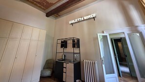 Ein Zimmer mit einer dekorativ verzierten Decke, einem Schild mit der Aufschrift 'CIVILETTA ROMEO', einem Heizkörper, einem kleinen Schreibtisch mit Wasserkocher und einem Stuhl.