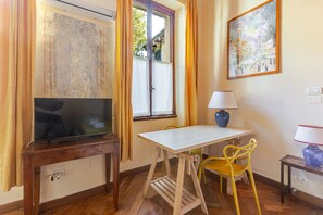 Ein Zimmer mit Fernseher auf einem Holzboden, einem Tisch mit Lampe und zwei gelben Stühlen.