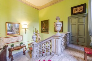 Una escalera con barandillas ornamentales, un espejo, una estatua y un cuadro enmarcado en la pared.