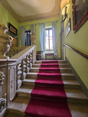 A grand staircase with a red carpet, ornate balustrade, and a view of a room with a window and curtains. - CASA MIA (Verona)