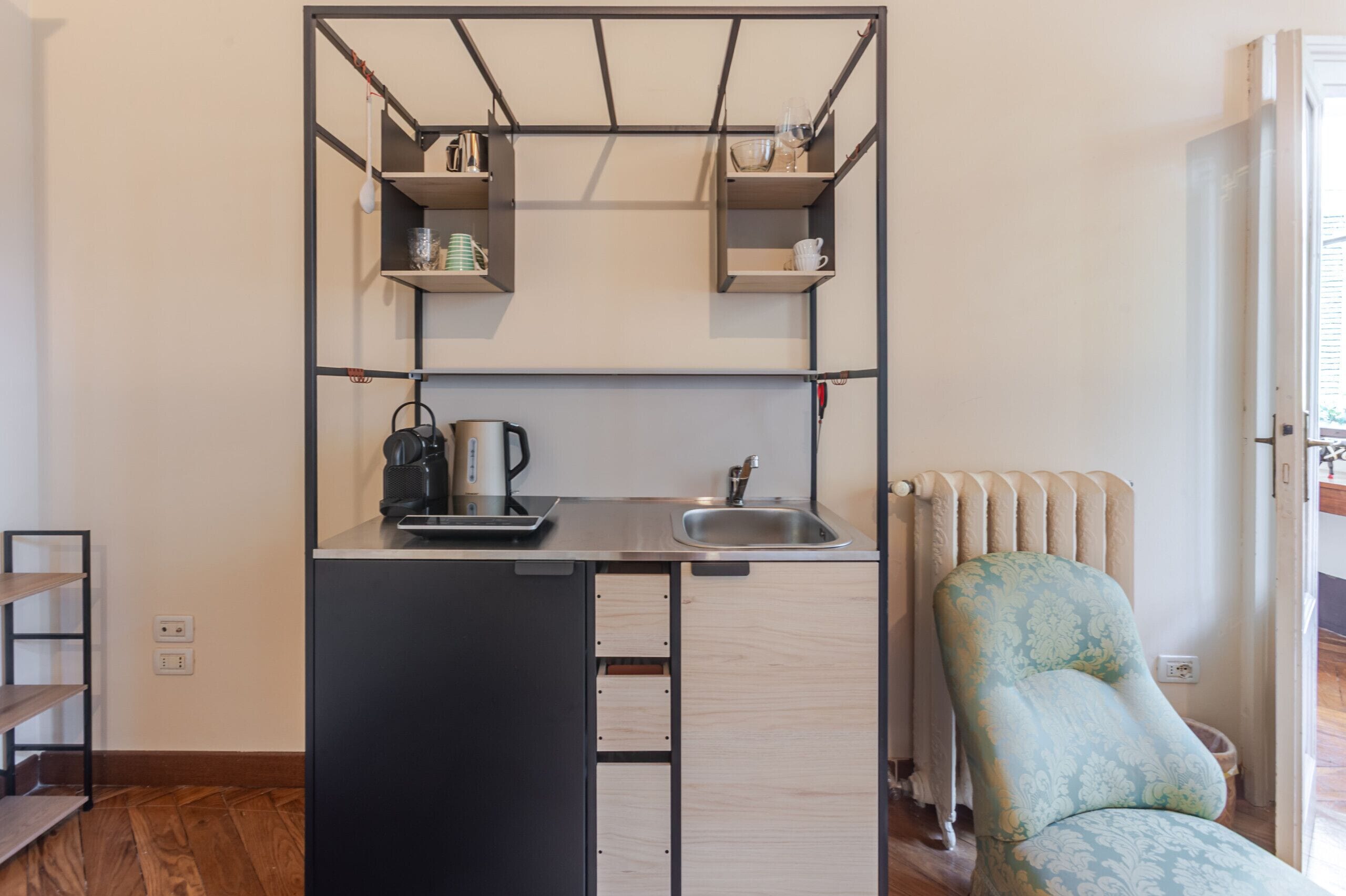 Een compacte kitchenette met een koffiezetapparaat, waterkoker en een klein spoelbakje.