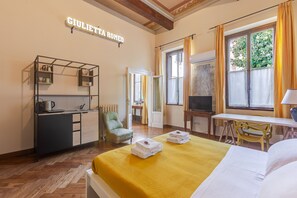 Habitación de hotel con cama, escritorio, televisión, armario y ventana con cortinas.