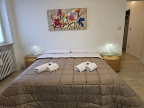 A hotel room with a bed, two bedside tables, a painting on the wall, and a radiator. - Accogliente CASA DIONIGI a Verona (Verona)
