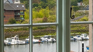 A view through a window of a marina with boats docked, a building with a balcony, and greenery in the background. - Central Boutique 2 Bed Cottage – Sleeps 6 (Lymington)