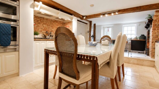 A dining area with a glass table, wooden chairs, and a brick wall. - Central Boutique 2 Bed Cottage – Sleeps 6 (Lymington)