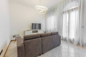 A modern living room with a grey sofa, a flat-screen TV on a white cabinet, and sheer curtains. - -Stanza con bagno privato 8 - uso cucina -Bastioni (Verona)